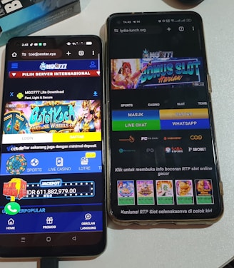 Two smartphones are displayed on a white surface, both showing gambling websites with colorful graphics, text, and various options for logging in and accessing games. The screens are bright and filled with promotional content related to casino and slot games.
